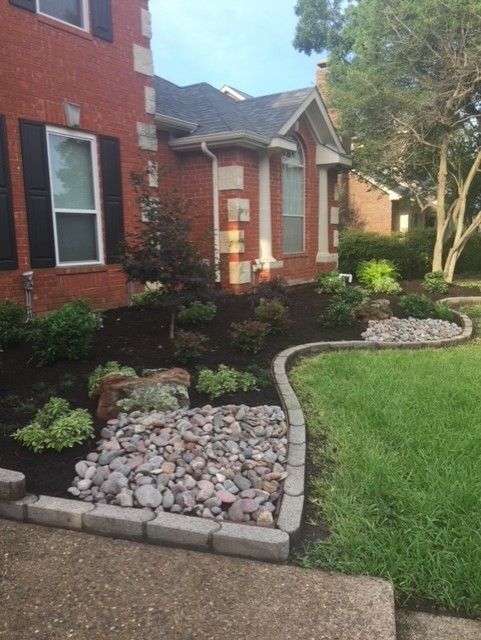 Brick house with landscaped front yard, featuring mulch, rocks, and green grass.