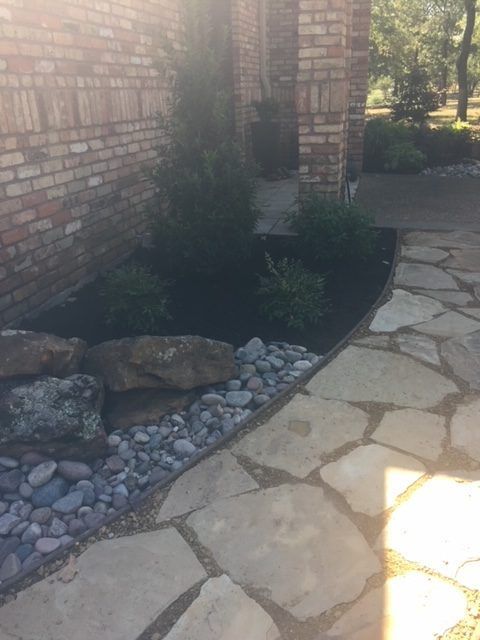 Stone walkway with a brick wall, garden bed with rocks and plants.
