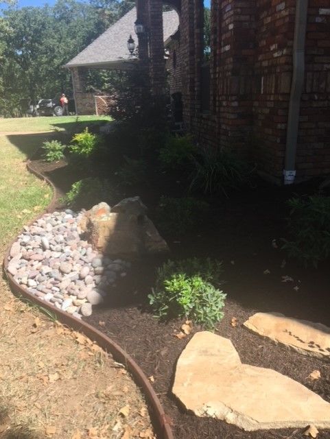 Landscaped garden bed with rocks and mulch, next to a brick house.