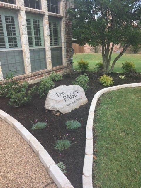 A stone sign in a landscaped yard reads 