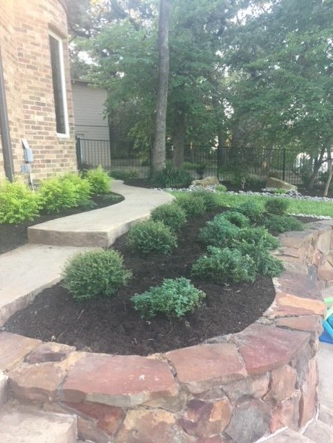 Landscaped front yard with path, stone wall, shrubs, and mulch.