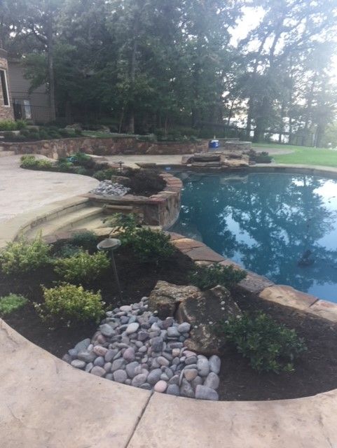 Pool with stone edge, landscaping, and trees in background.