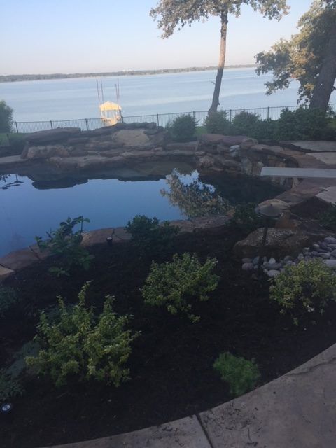 A landscaped backyard with a pool overlooking a lake. Plants and rocks surround the pool.
