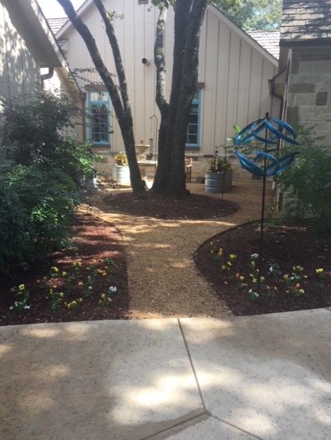Gravel path leads to a backyard with a tree, flowerbeds, and a building.