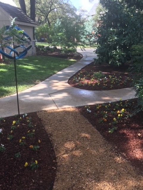 Concrete and gravel pathways through a garden with flower beds and trees.