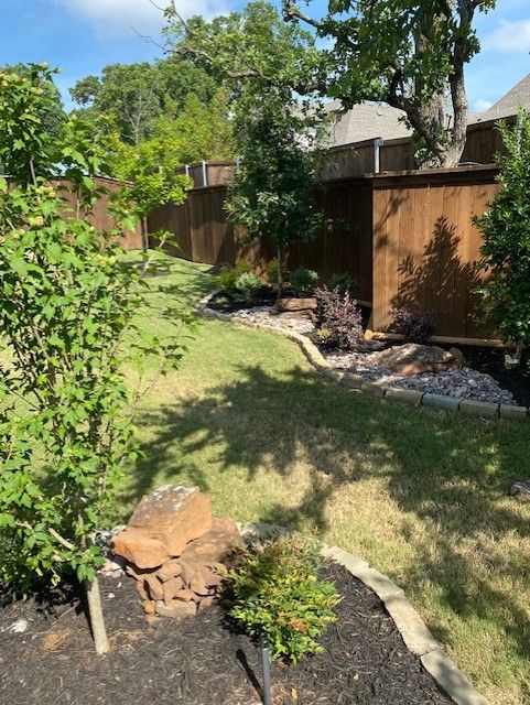 A backyard with a brown wooden fence, landscaping, and a lawn on a sunny day.