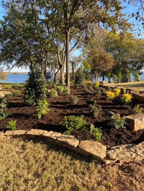 Landscaped garden bed with mulch, shrubs, and a lake backdrop.