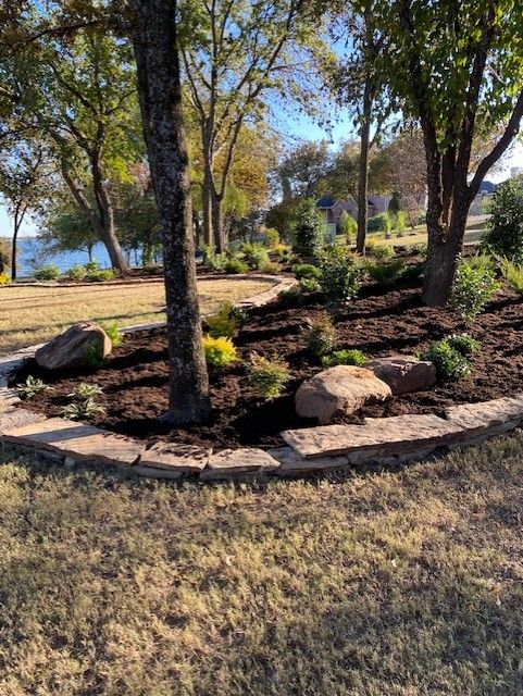 Landscaped garden bed with trees, rocks, and brown mulch against lake view.