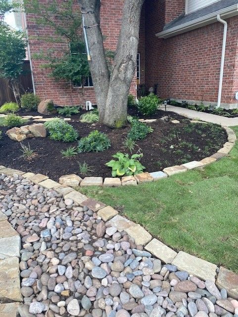 Landscaped front yard with a rock border, mulched beds, and a tree.