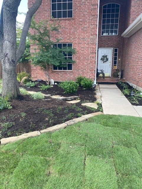 A brick house with a lawn being re-sodded. A stone path leads to the front door; dark mulch in the flower beds.