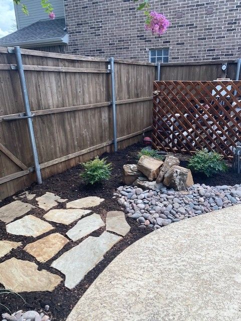 Flagstone path and rock garden next to a wooden fence and patio.