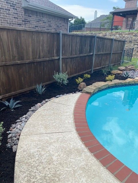 Poolside garden with brown fence, walkway, pool, and various plants.