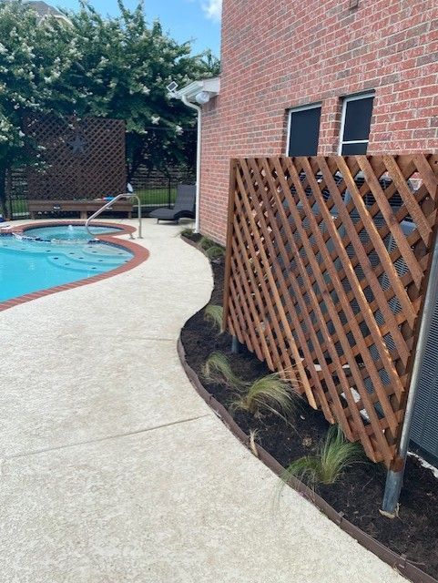 A backyard with a pool, wooden lattice, brick building, and landscaped walkway.
