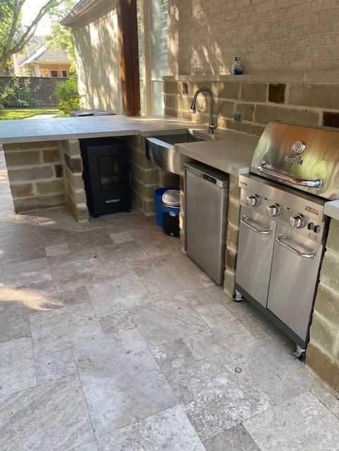 Outdoor kitchen with grill, sink, and countertop made of brick and stone.