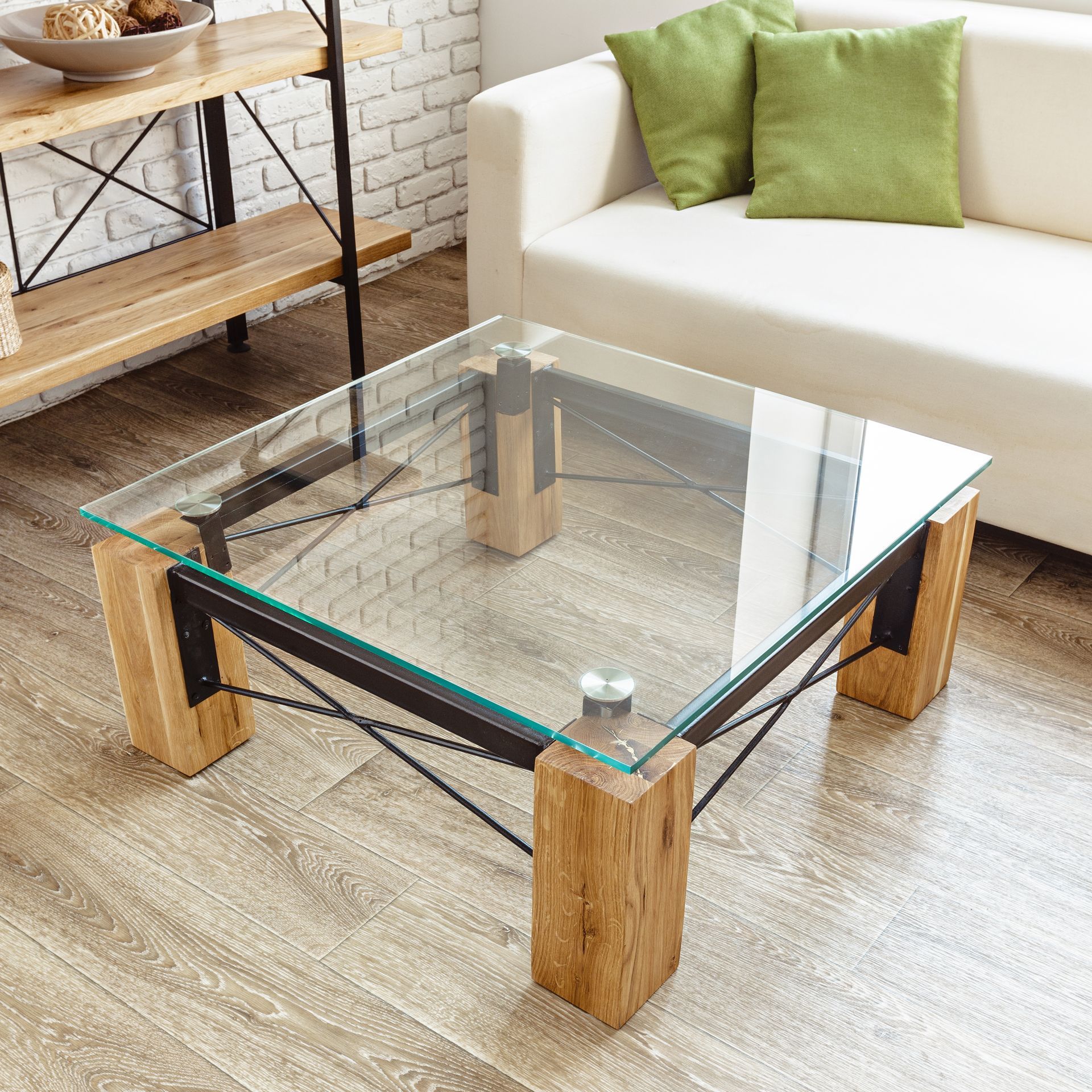 Modern glass coffee table with wooden legs in a bright living room beside a white sofa with green pillows