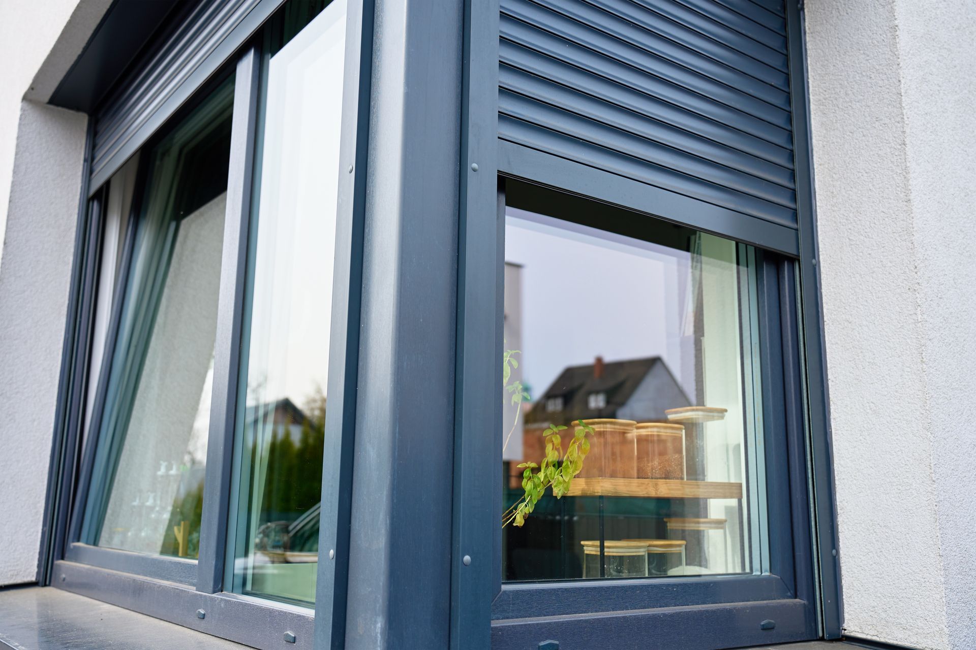 Modern gray house window with green shutters reflecting a balcony and building exterior