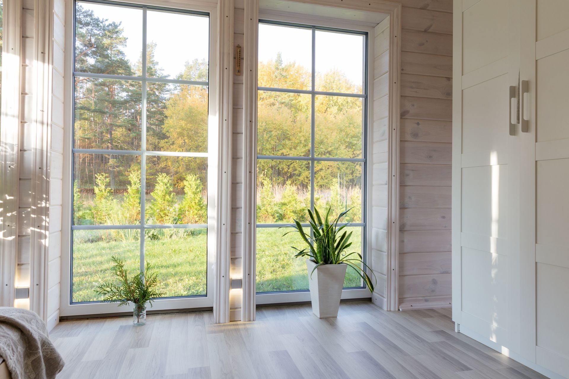 Bright room with floor-to-ceiling windows, white cabinets, and a potted plant overlooking a green garden