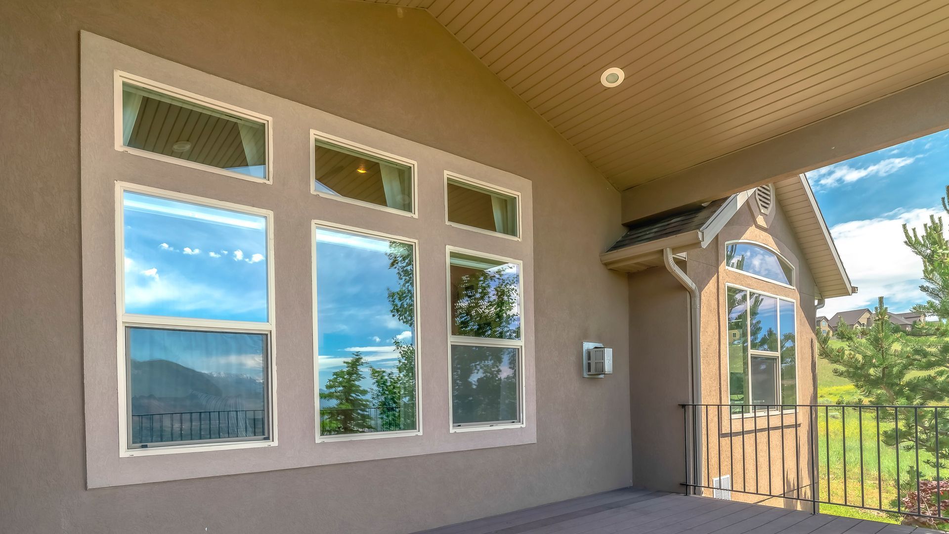 Covered patio with beige walls, white-trimmed windows, and a metal gate overlooking mountains and blue sky