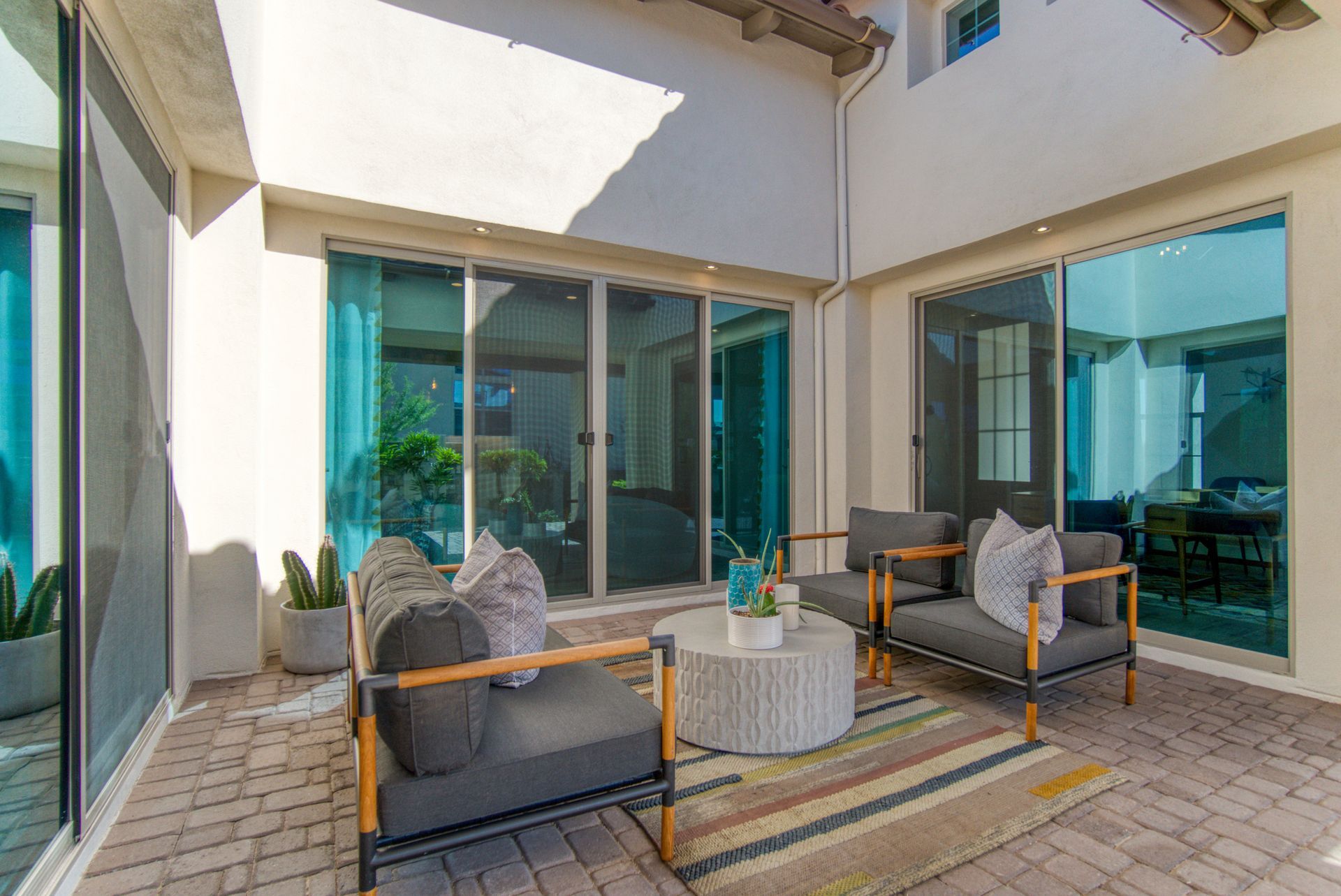 Patio seating area with wicker chairs, round table, and sliding glass doors under a covered courtyard.