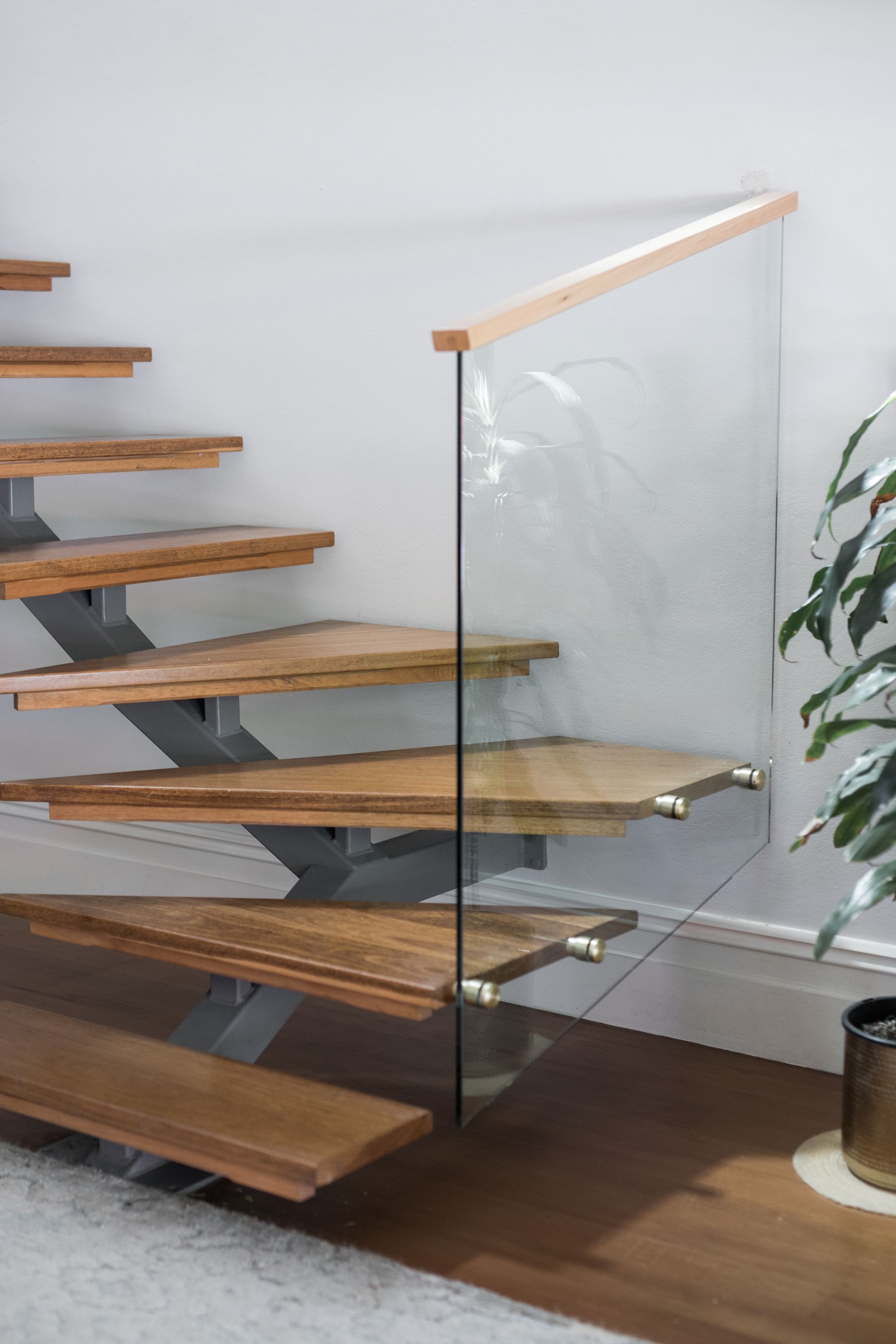 Modern floating wooden staircase with glass railing and white wall