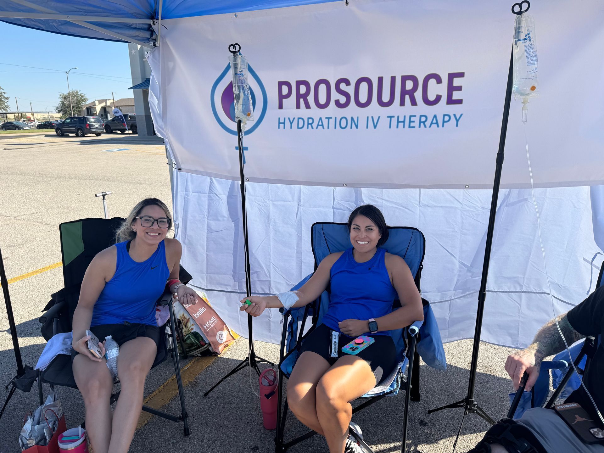 Two women getting IV hydration therapy under a canopy with the