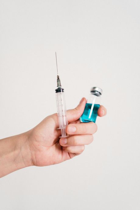 Hand holding a syringe and a vial of blue liquid, likely for injection.