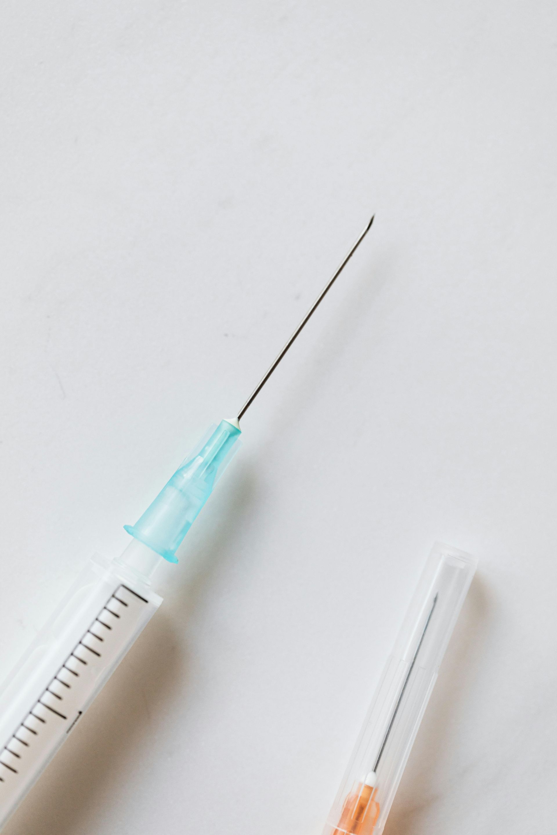 Syringe with needle, next to a detached needle cap, on a white surface.