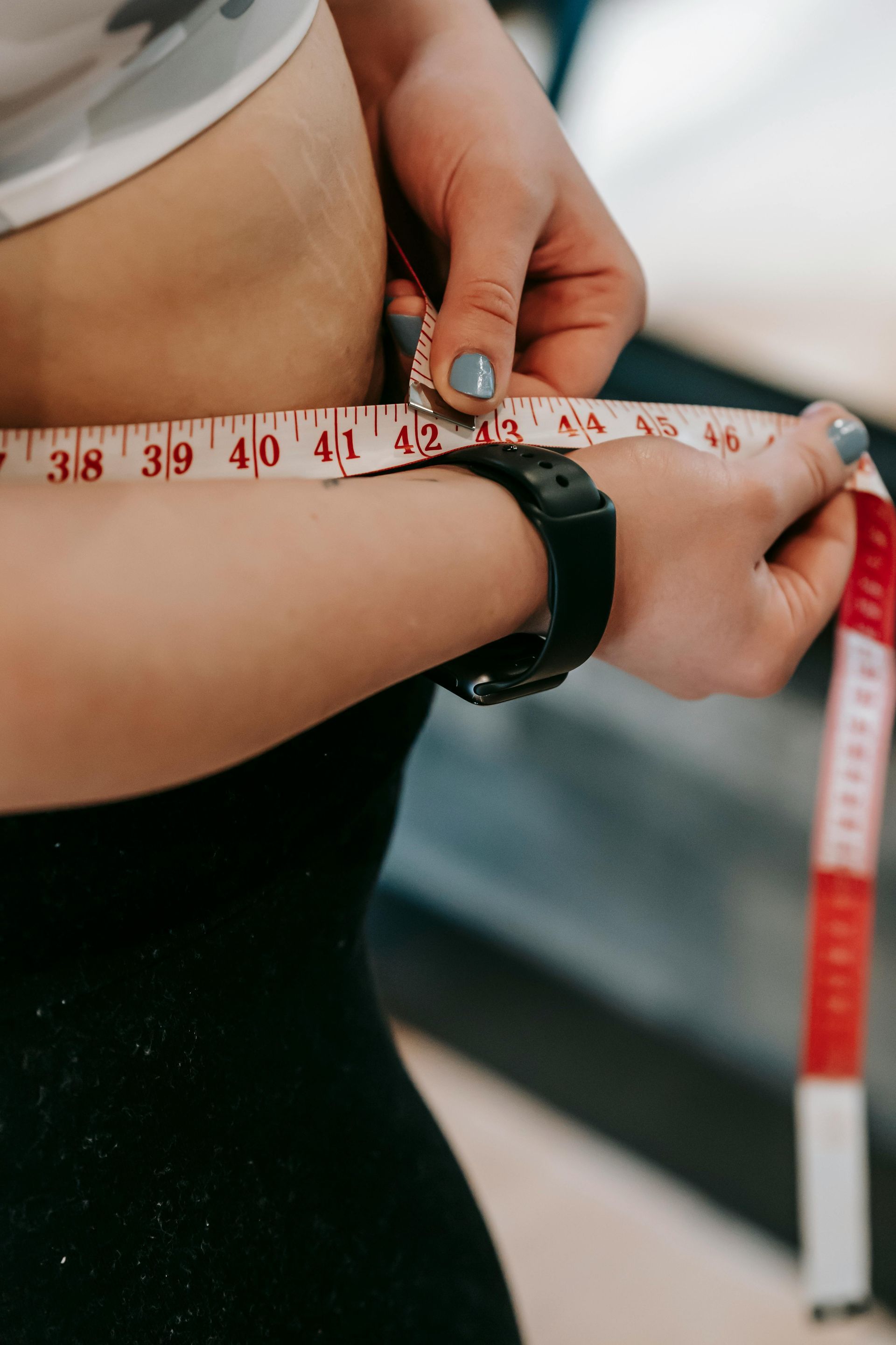 Person measuring waist with red and white measuring tape.