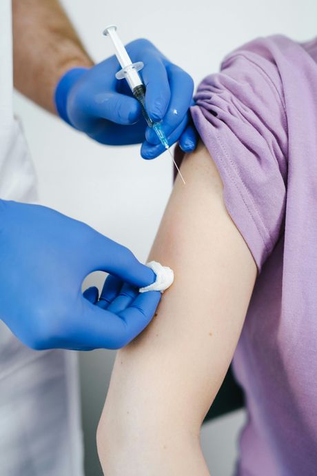 Person receiving an injection in the arm from a person wearing blue gloves and a white coat.