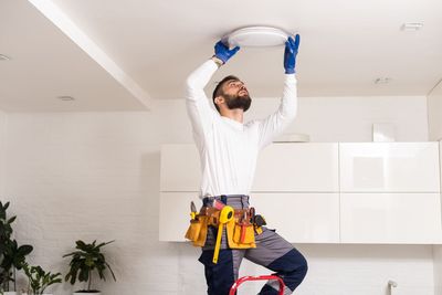 A man is standing on a ladder fixing a light fixture on the ceiling.