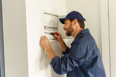 A man is working on an electrical box on a wall.