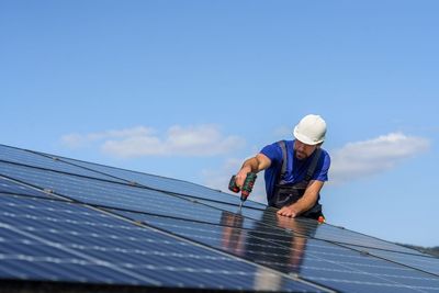 A man is installing solar panels on the roof of a building.