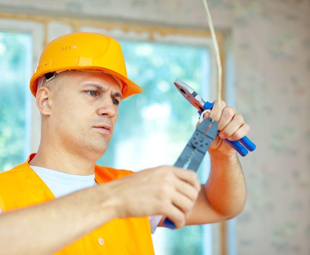 A man wearing a hard hat is cutting a wire with pliers.