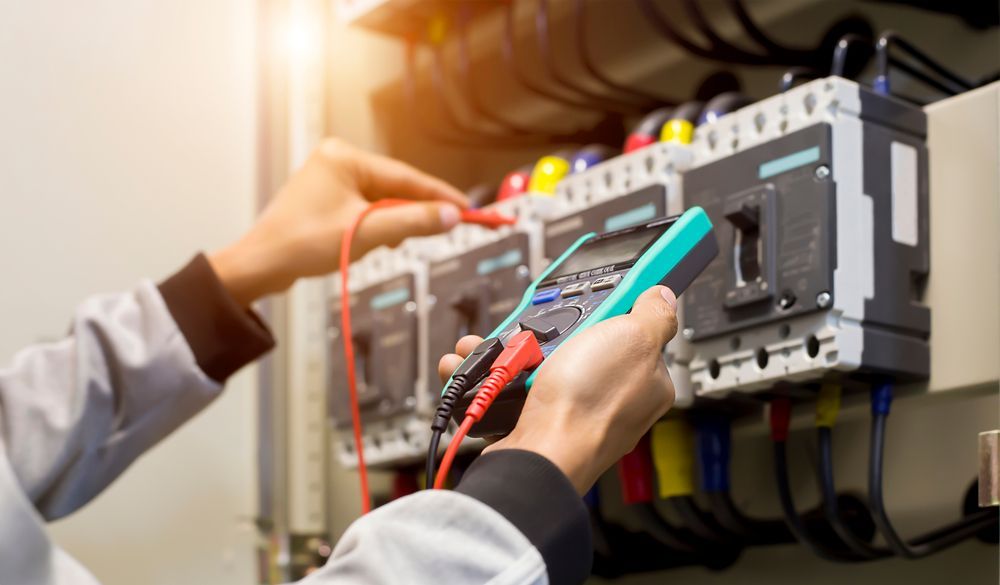 An electrician is working on an electrical box with a multimeter.