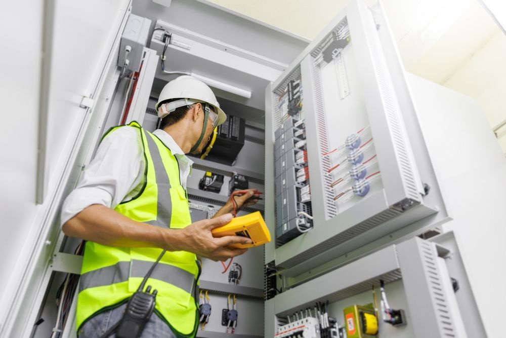 A man in a yellow vest is working on an electrical box.