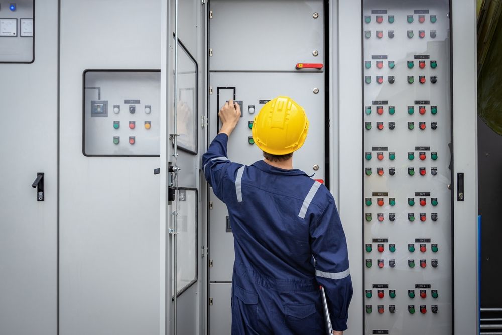 A man in a hard hat is working on a control panel.