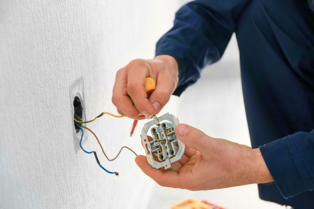 A man is fixing an electrical outlet with a screwdriver.