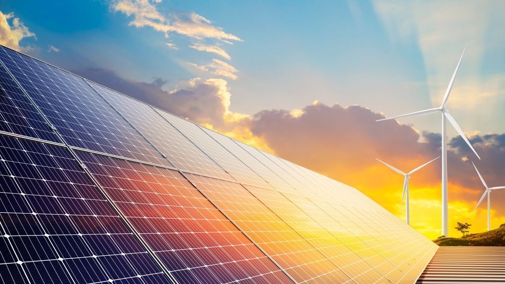 A row of solar panels and wind turbines at sunset.