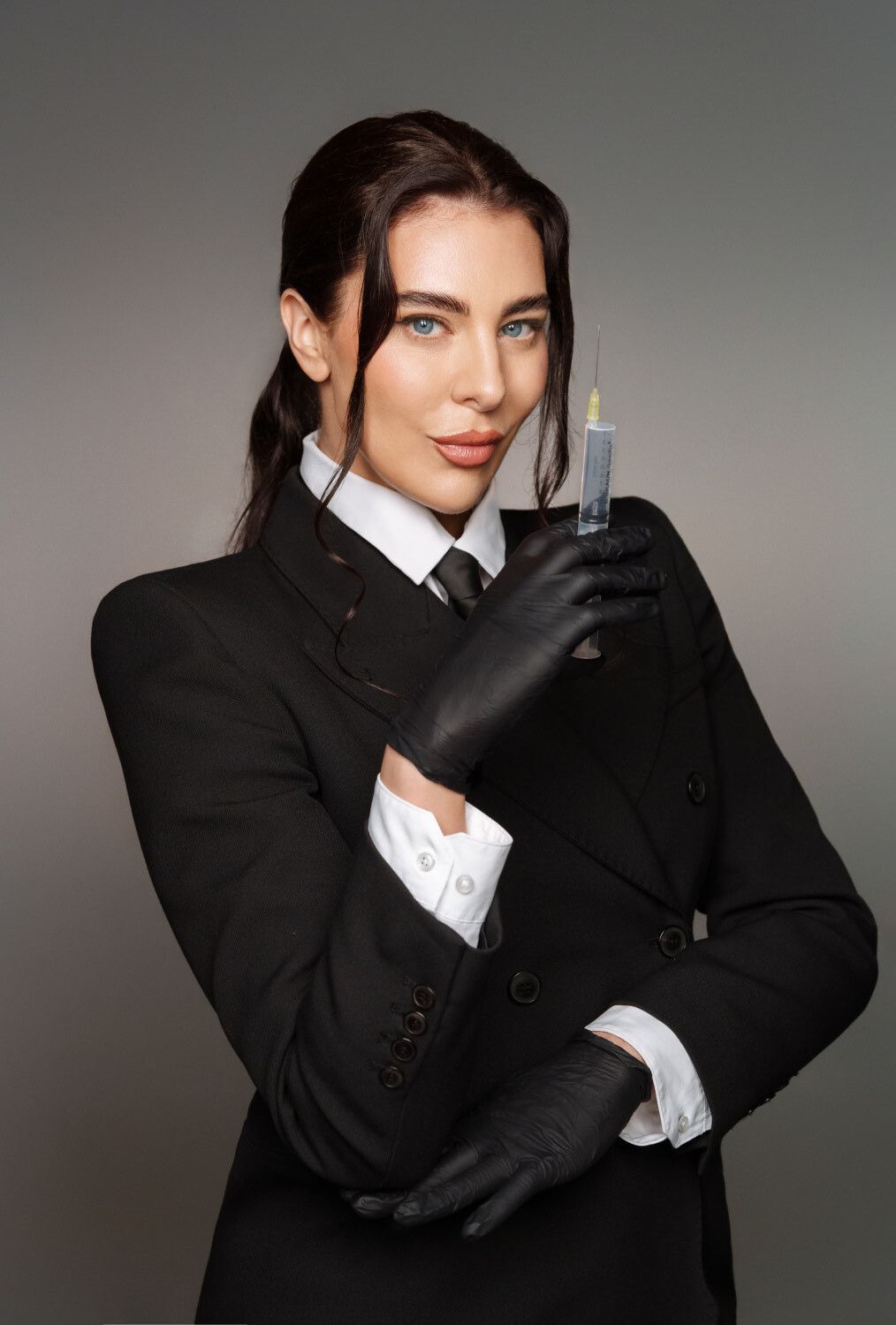 Frau im weißen Kittel hält Spritze und lächelt in die Kamera.