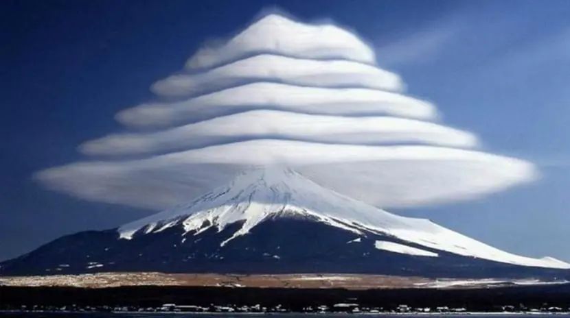 Mount Fuji with layered lenticular clouds. Snowy peak, blue sky.
