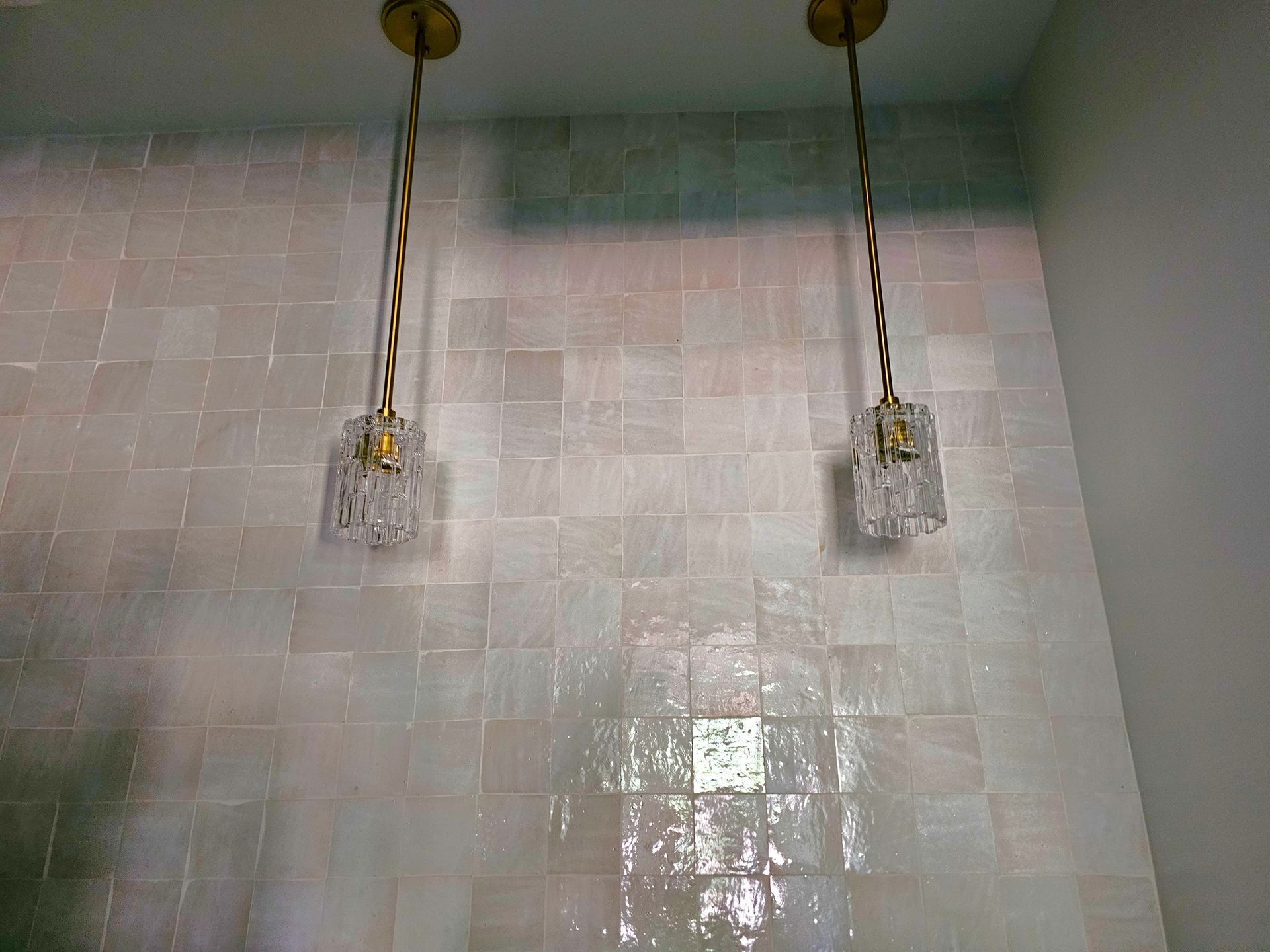Two showerheads mounted above a tiled shower wall with water running down the tiles