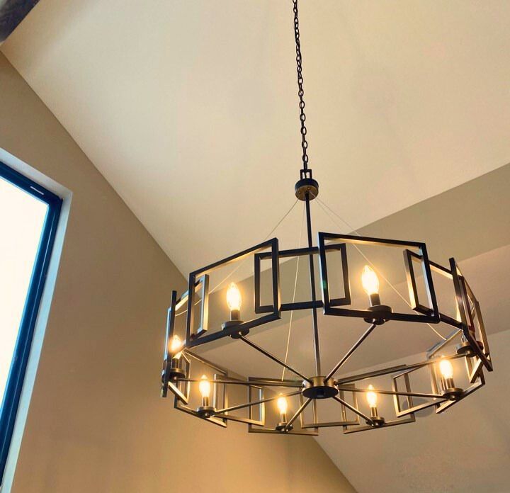 Black metal chandelier with lit bulbs hanging from a ceiling in a beige room
