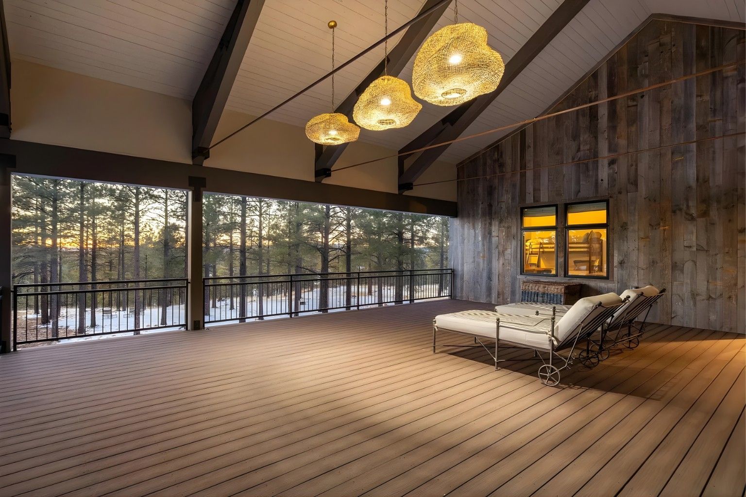 Spacious modern living room with large windows, wood walls, hanging lights, and a white chaise lounge