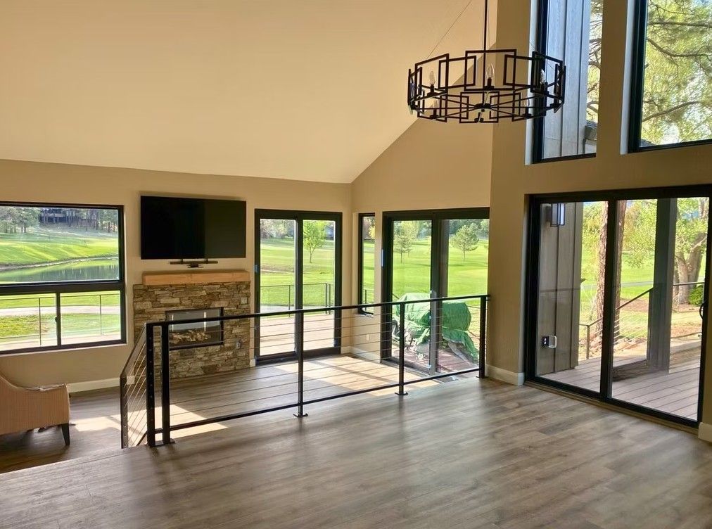 Bright living room with large windows, high ceilings, fireplace, and glass doors overlooking greenery