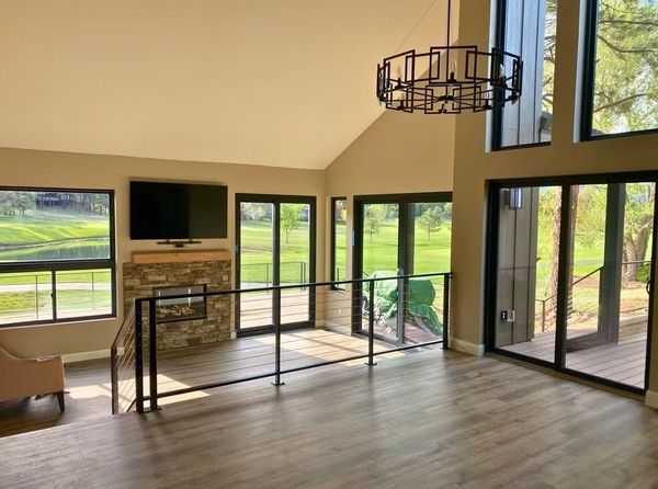 Modern living room with large windows, fireplace, TV, and stairs overlooking a green landscape