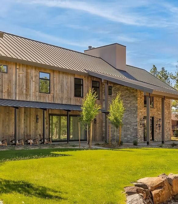 Modern two-story house with wood siding, large windows, and a green lawn under a blue sky
