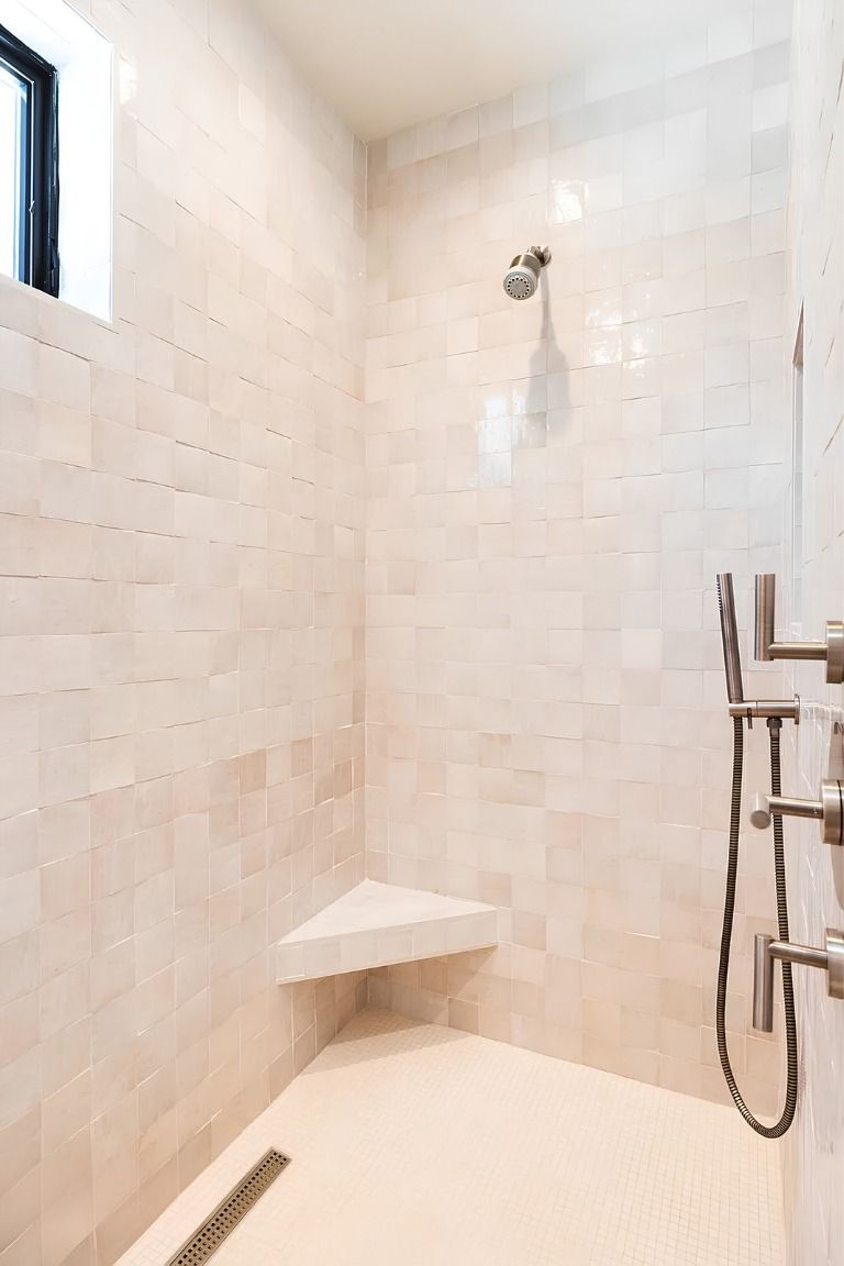 White tiled shower stall with a corner shelf, showerhead, and handheld shower sprayer