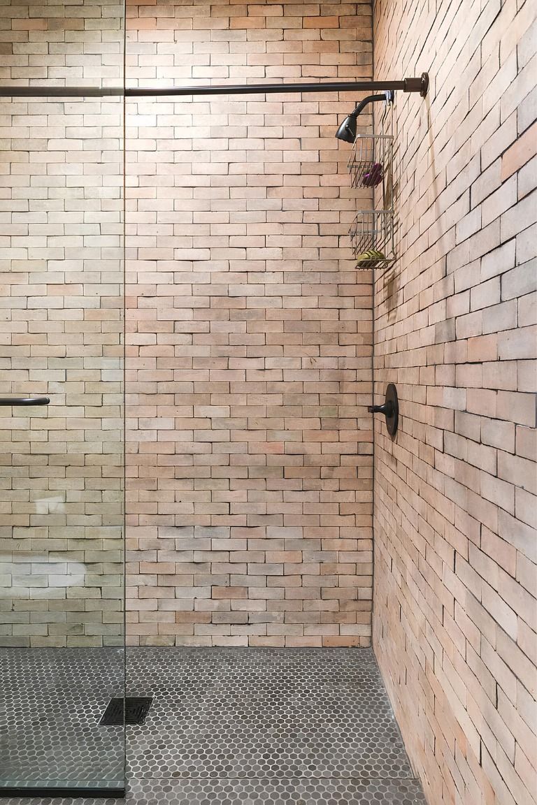 Modern bathroom shower with glass partition, brick walls, and gray tiled floor