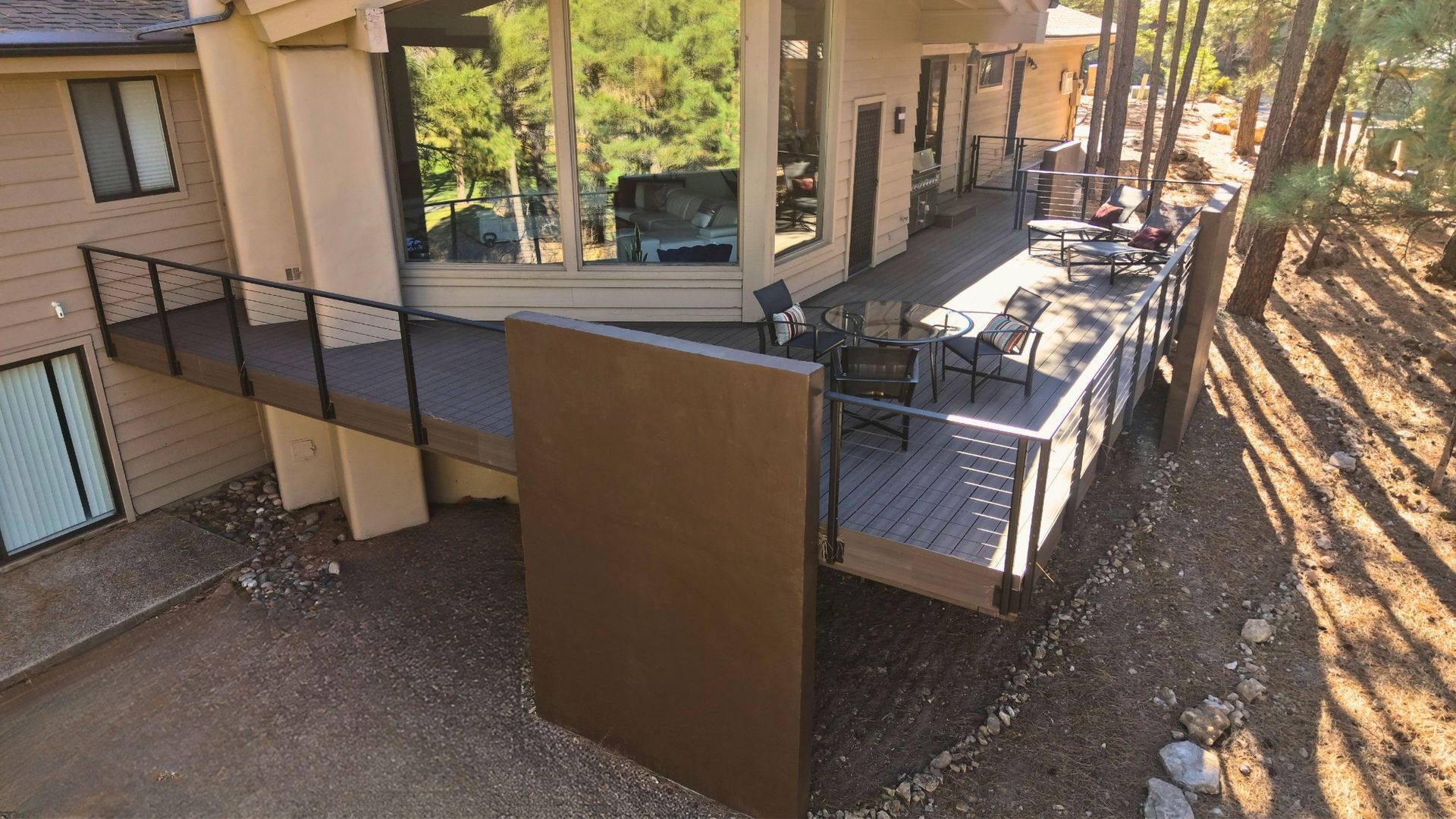 Apartment building deck with stairs, railing, and outdoor seating overlooking a wooded slope.