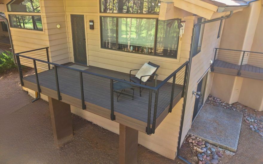 Small outdoor balcony with black railing, tan siding, and a table holding a folded chair.